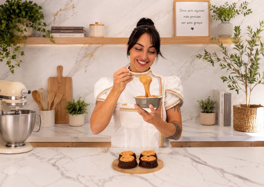 Natália sorrindo na cozinha enquanto prepara cupcakes com cobertura de confeitaria saudável