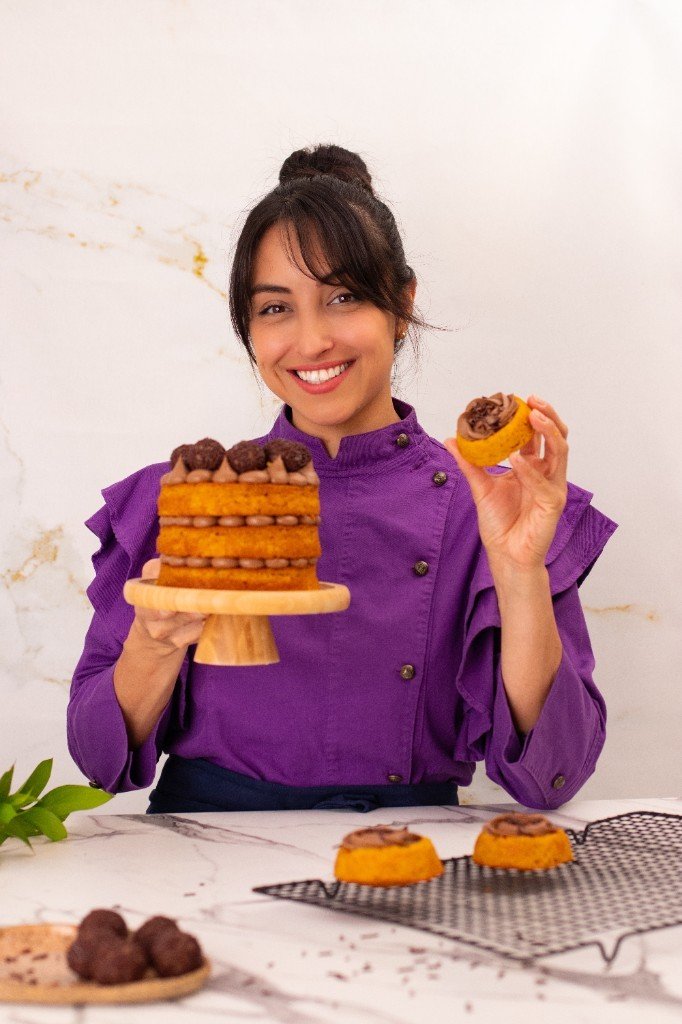 Nati, confeiteira da Escola de Confeitaria Saudável, com bolo e doces artesanais